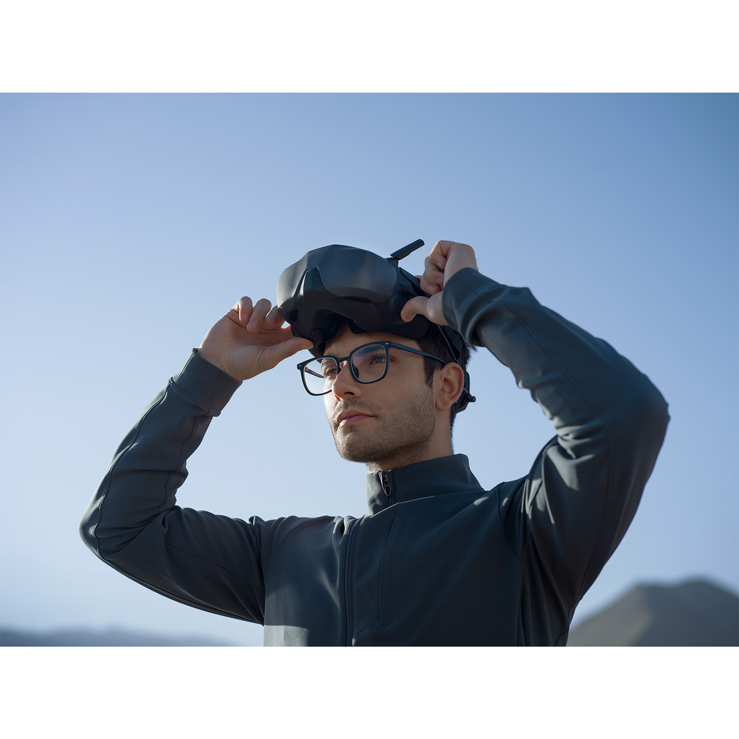 Uomo con visore VR, lo tiene contro un cielo blu.