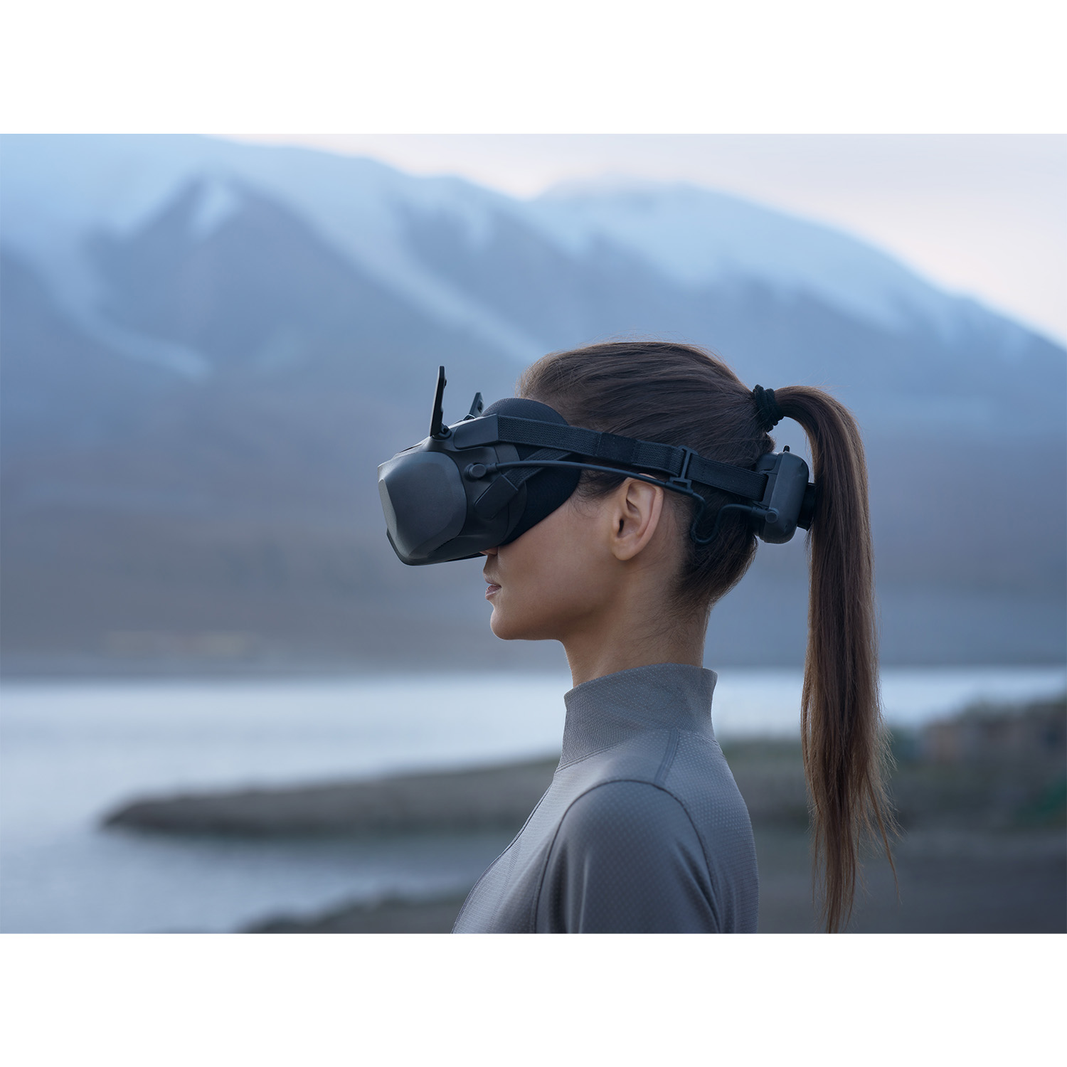 Una donna con un visore VR di fronte a un lago e montagne.