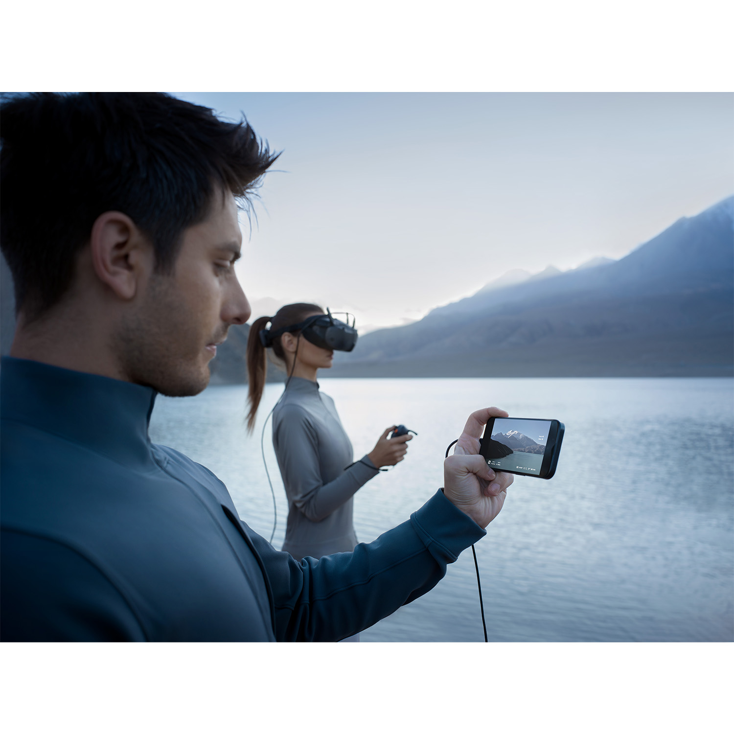 Due persone con visori VR. Uno tiene uno schermo, l'altro guarda il lago.