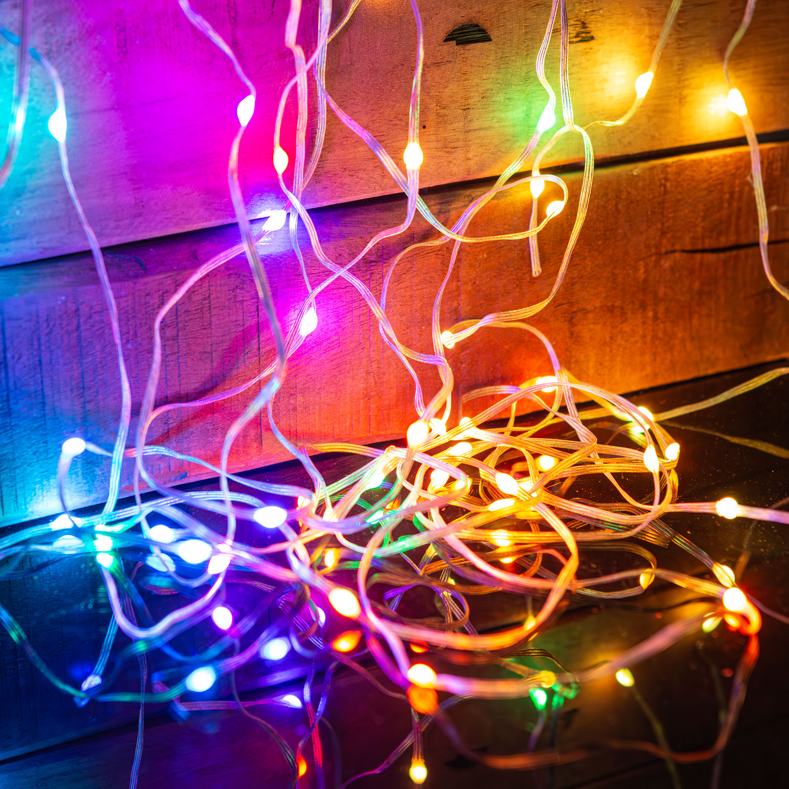 Színes LED-es fénysorok kuszasága fa felületen. Fekete felületen tükröződés.