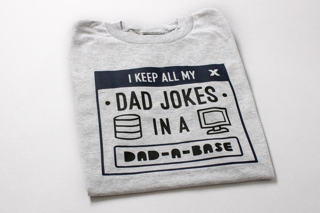 Ein graues T-Shirt mit dem Text 'I keep all my dad jokes in a Dad-a-base'.
