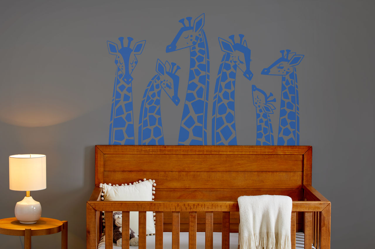 Giraffen-Wandtattoos über einem Holzbettchen. Graue Wand, weiße Bettwäsche.
