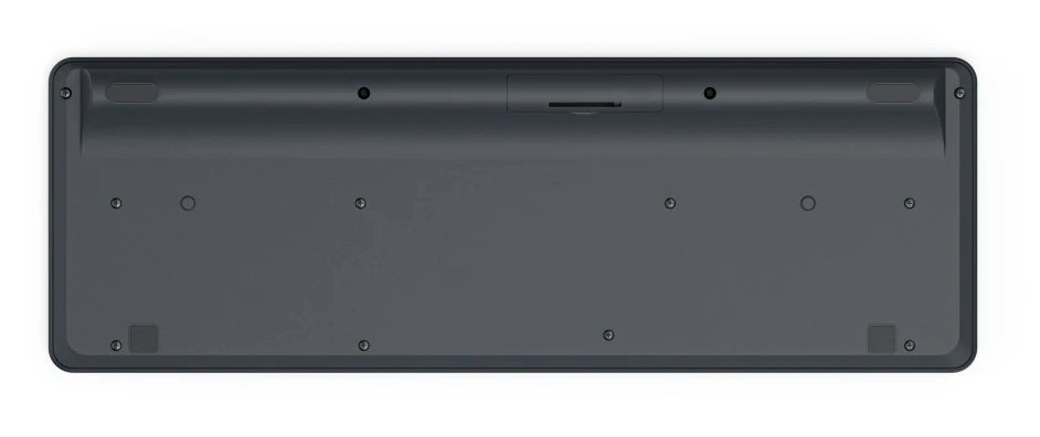 Spód klawiatury, ciemnoszary, ze śrubami i małą przegródką. Białe tło.