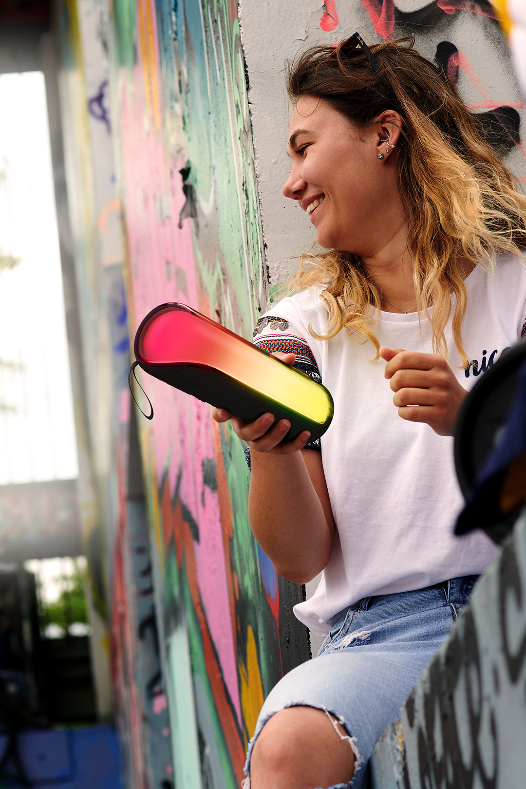 Nő hangszórót tart, mosolyog, graffitis fal előtt.