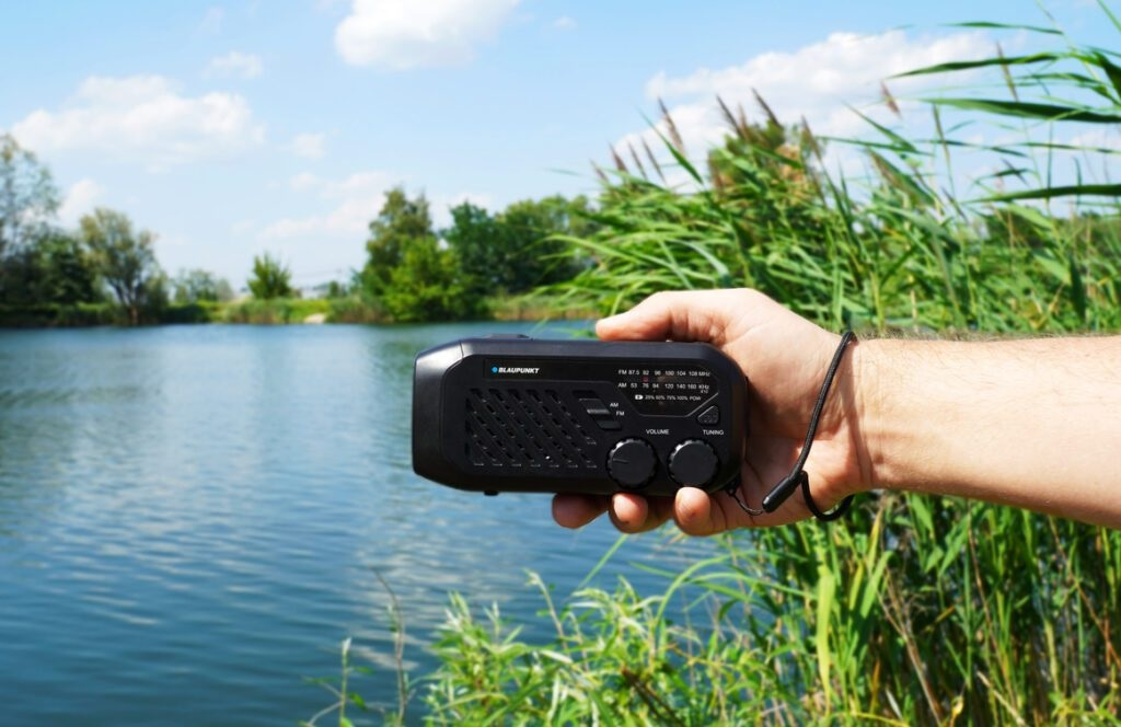 Ręka trzymająca czarne radio Blaupunkt, z jeziorem i drzewami w tle.