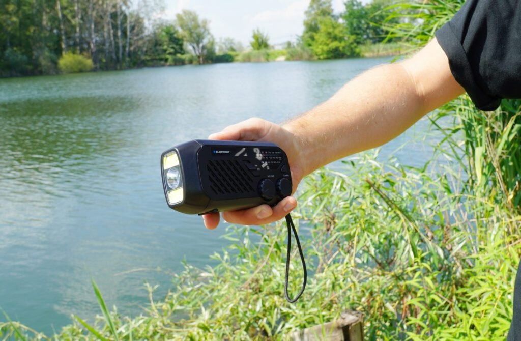 Czarne radio z jasnym światłem, trzymane przez dłoń nad wodą i trawą.