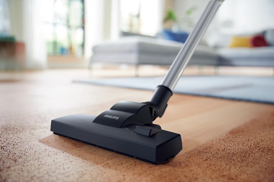 Głowica odkurzacza na drewnianej podłodze. Tło jest rozmyte, pokazując ustawienia salonu.