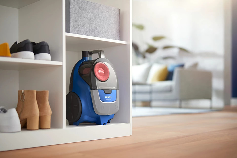 Niebiesko-szary odkurzacz Philips, przechowywany na białej półce szafki.