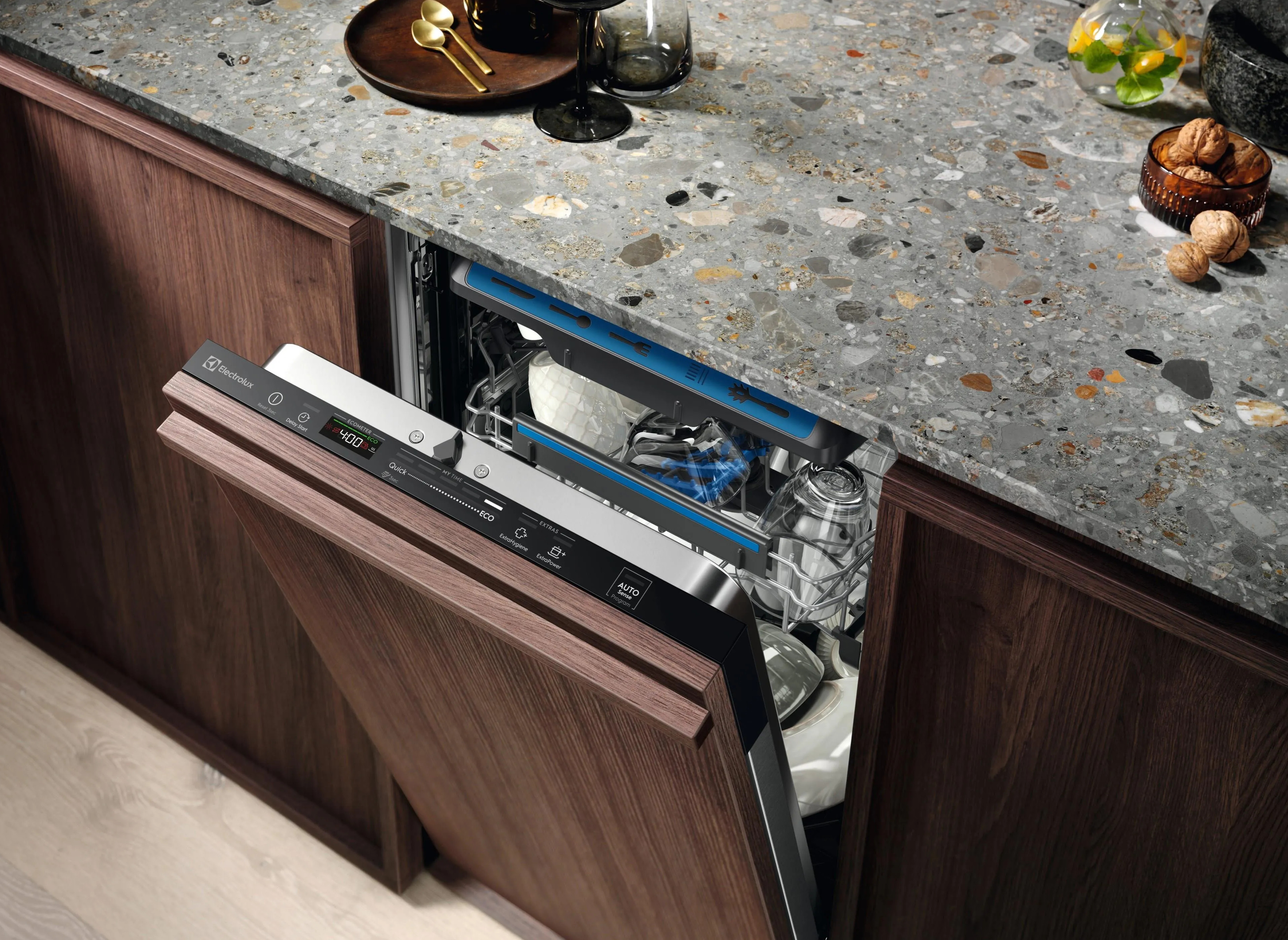 Zmywarka otwarta, pokazująca naczynia w środku. Drewniana szafka z granitowym blatem. Naturalne światło.