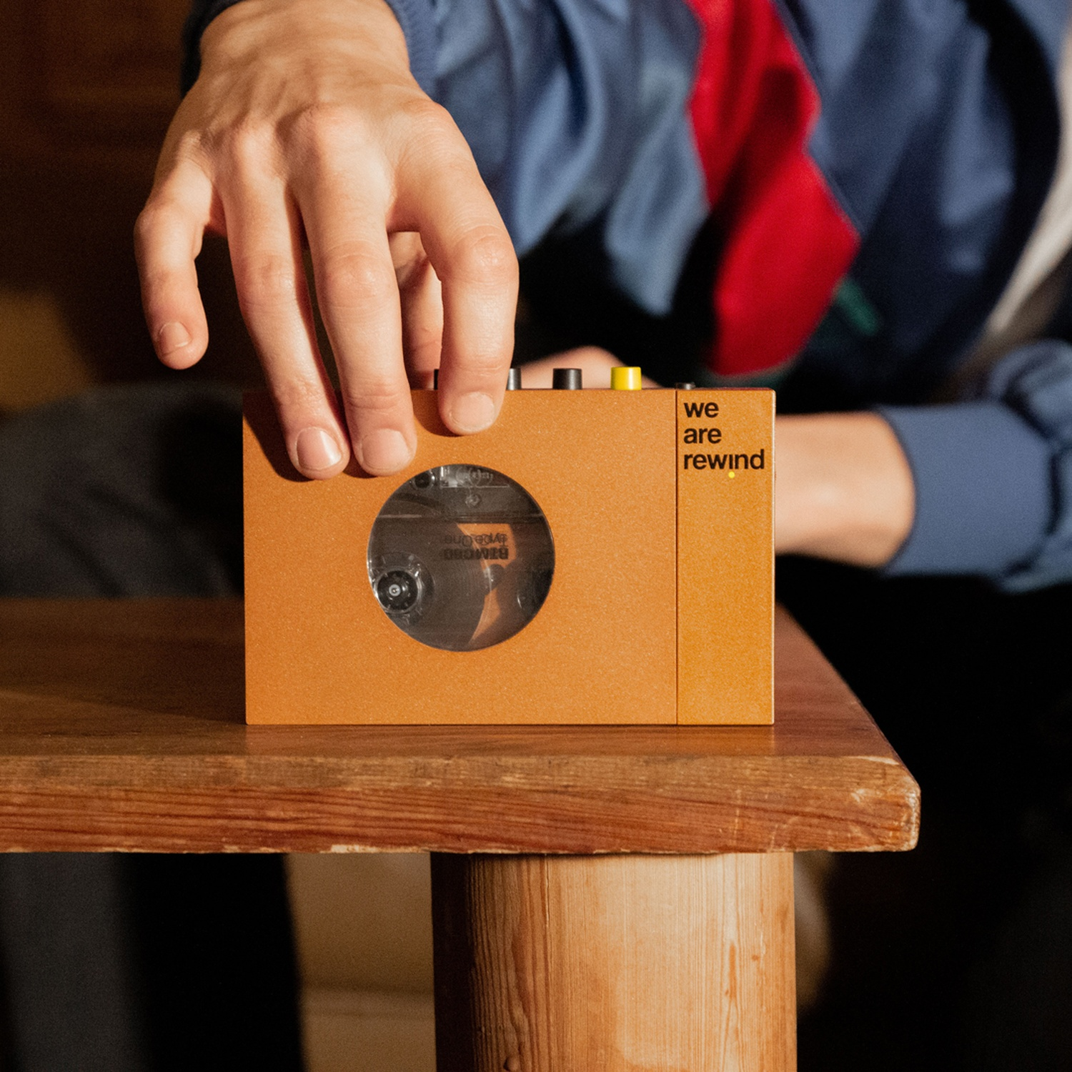 Un lettore di cassette arancione su un tavolo di legno. Mano che tiene una cassetta.