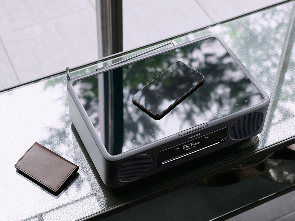 Nowoczesne radio z telefonem na górze i portfelem na szklanym stole. W tle okno.