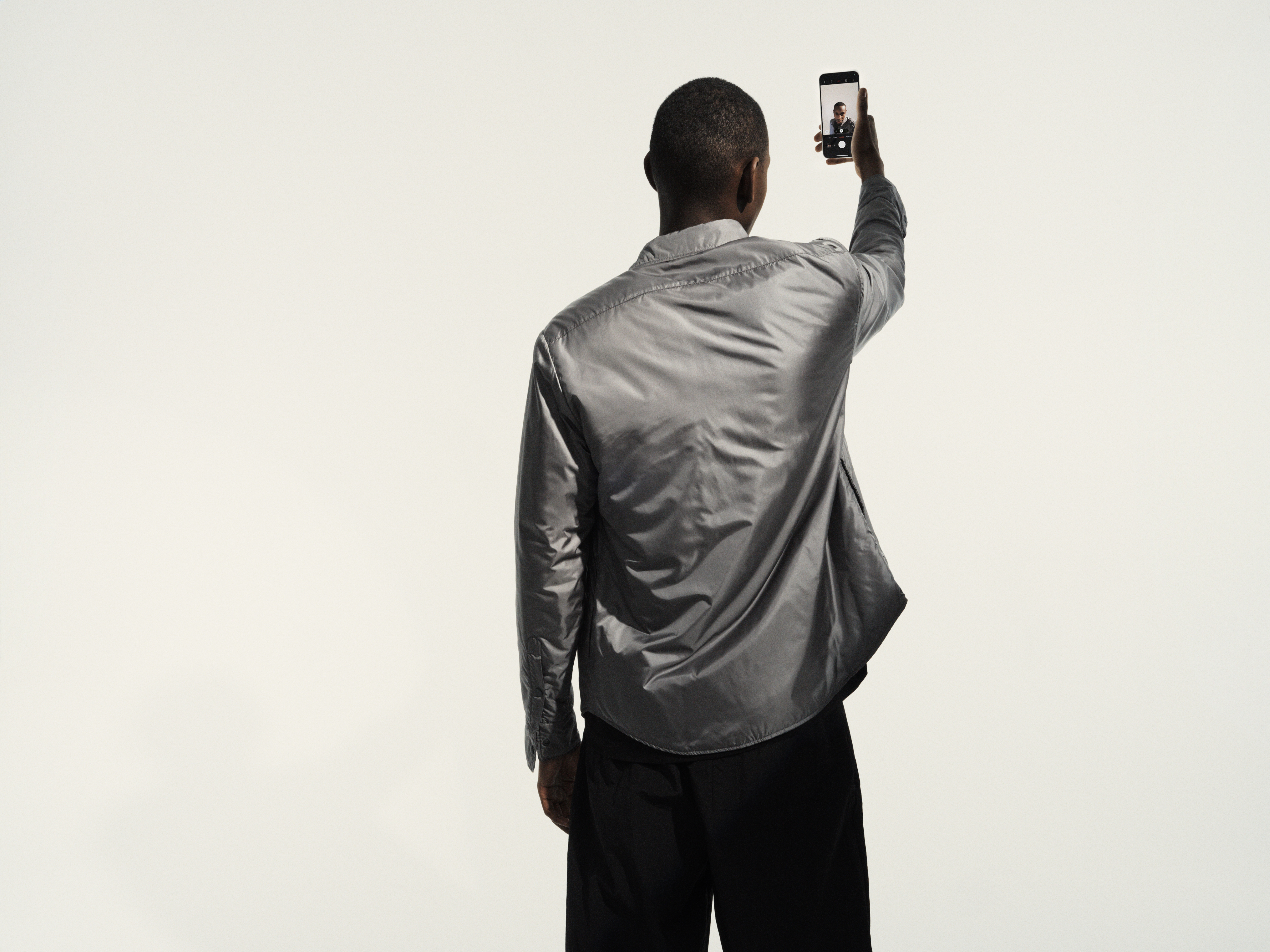 Eine Person in einem grauen Hemd macht ein Selfie mit einem Smartphone.