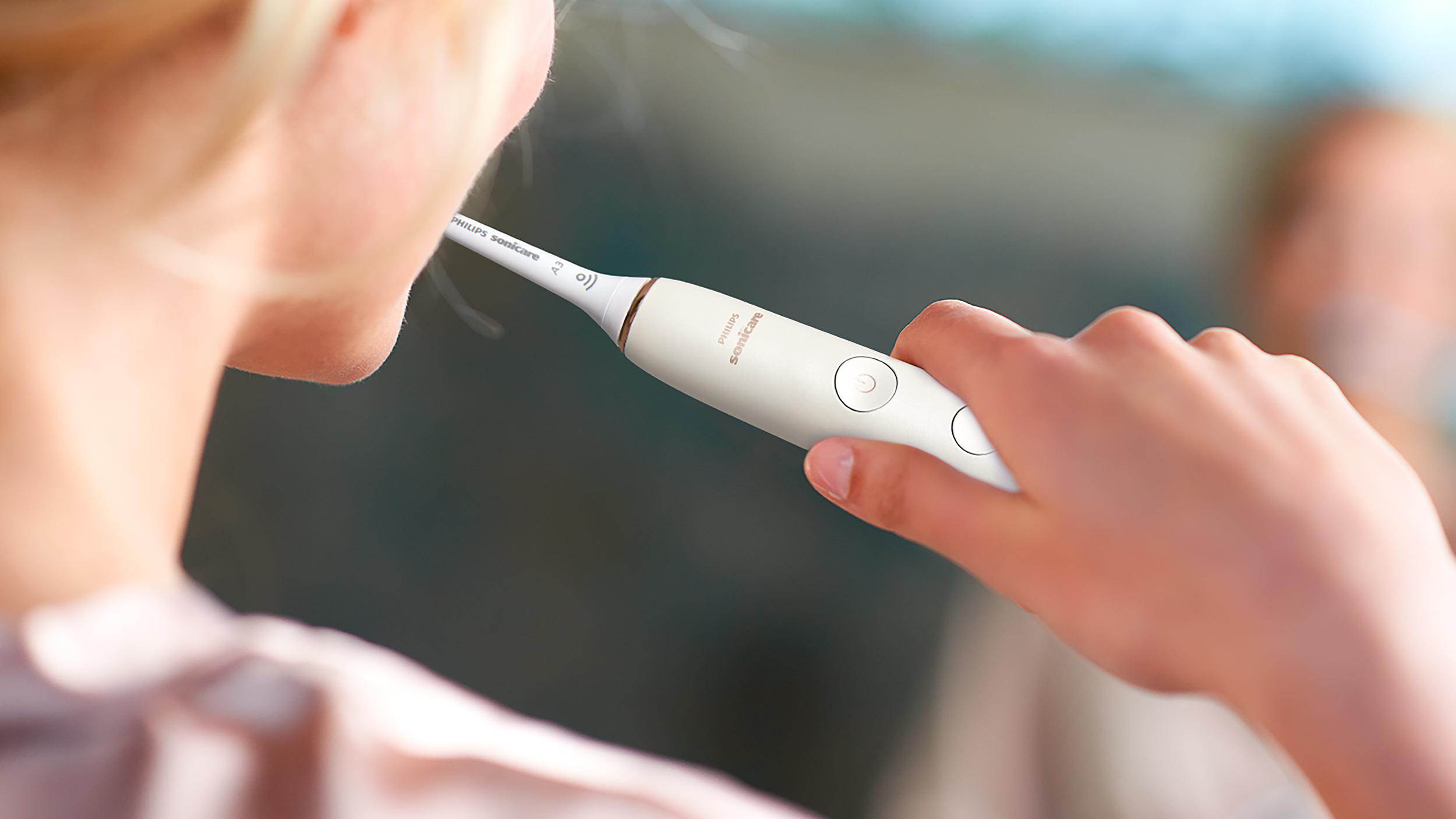 Frau putzt sich die Zähne mit weißer Zahnbürste, von hinten gesehen.
