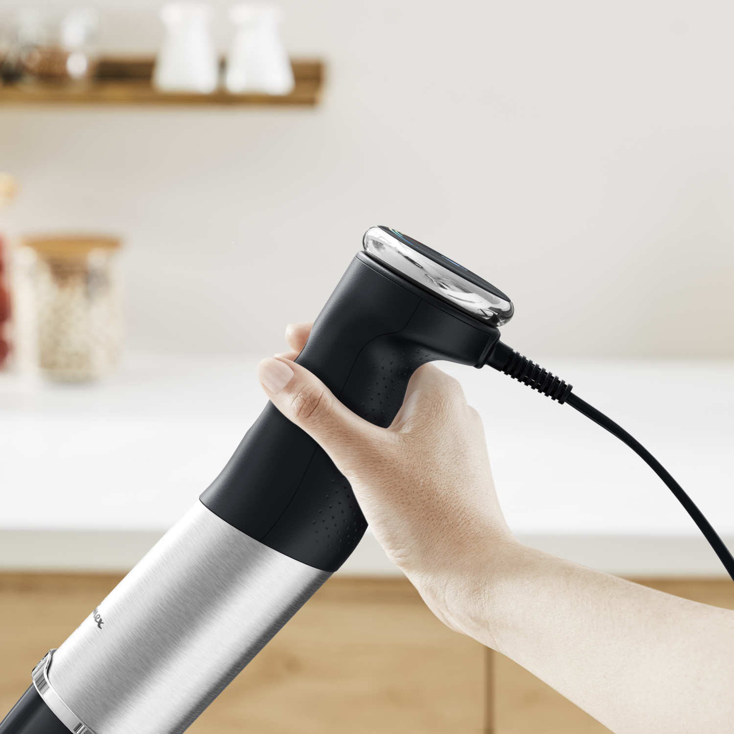 Een hand die een zwart en zilveren keukenapparaat vasthoudt, mogelijk een blender.