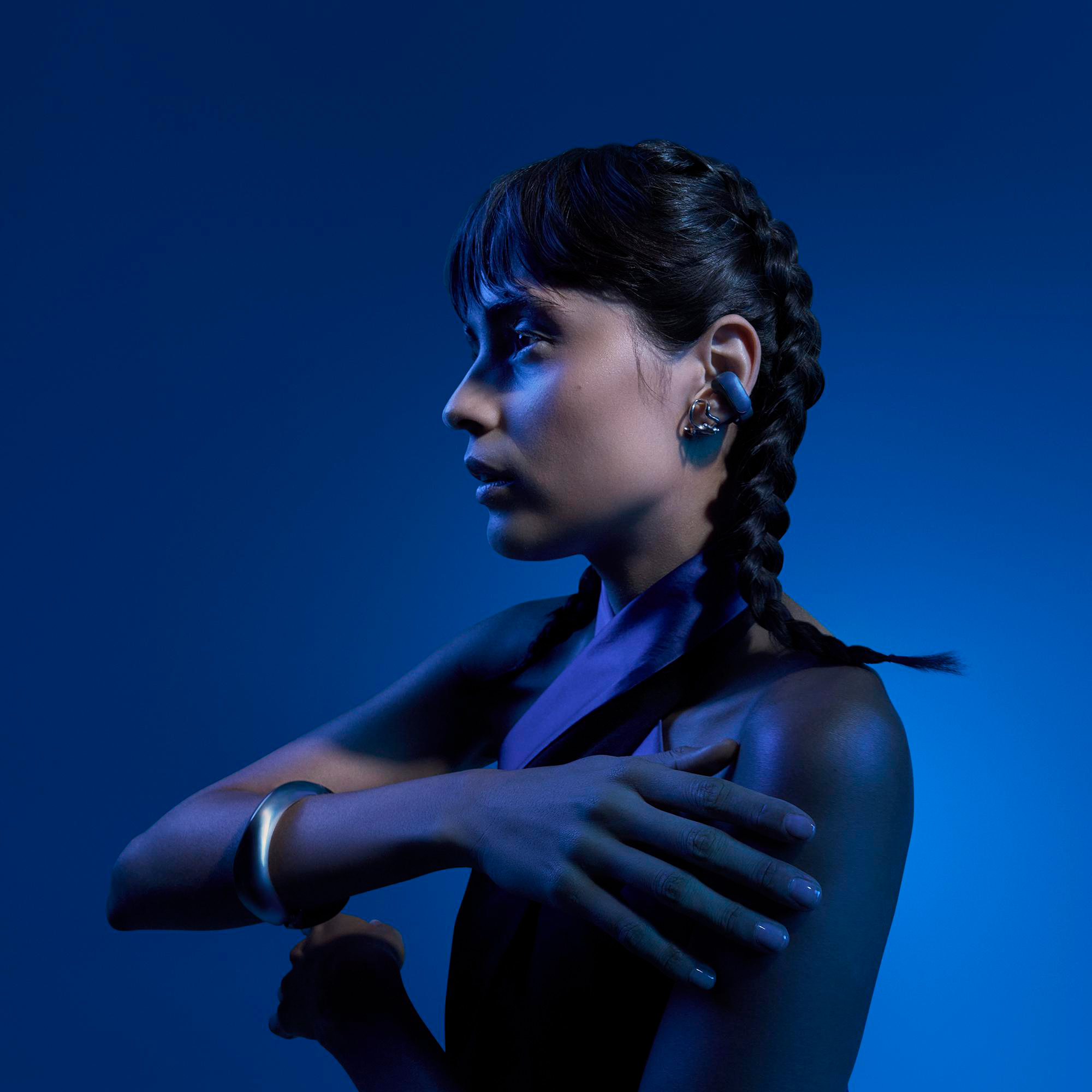 Frau im Profil mit geflochtenen Haaren, blaue Beleuchtung, Armschmuck.