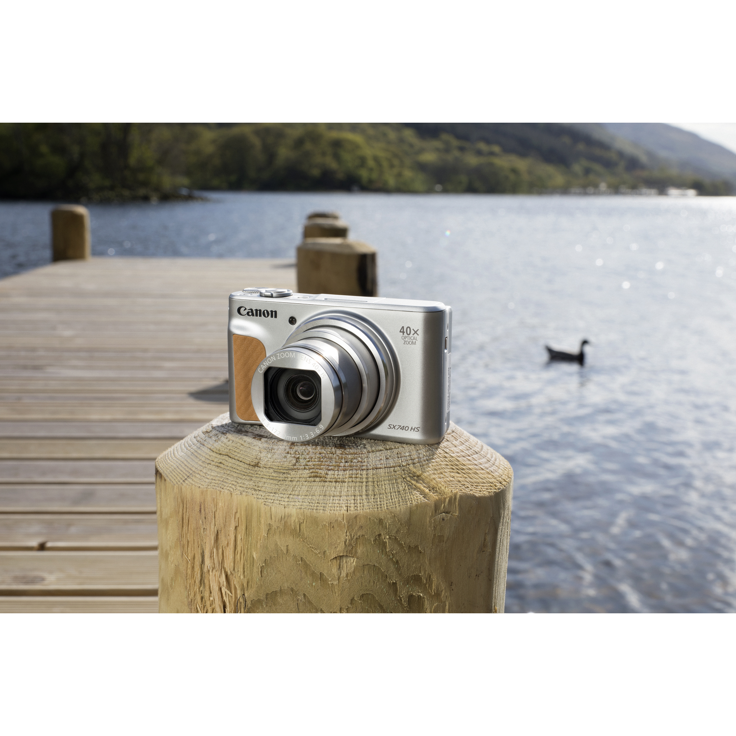 Canon camera on a wooden post overlooking a lake. A duck floats in the water. Mountains are in the background.