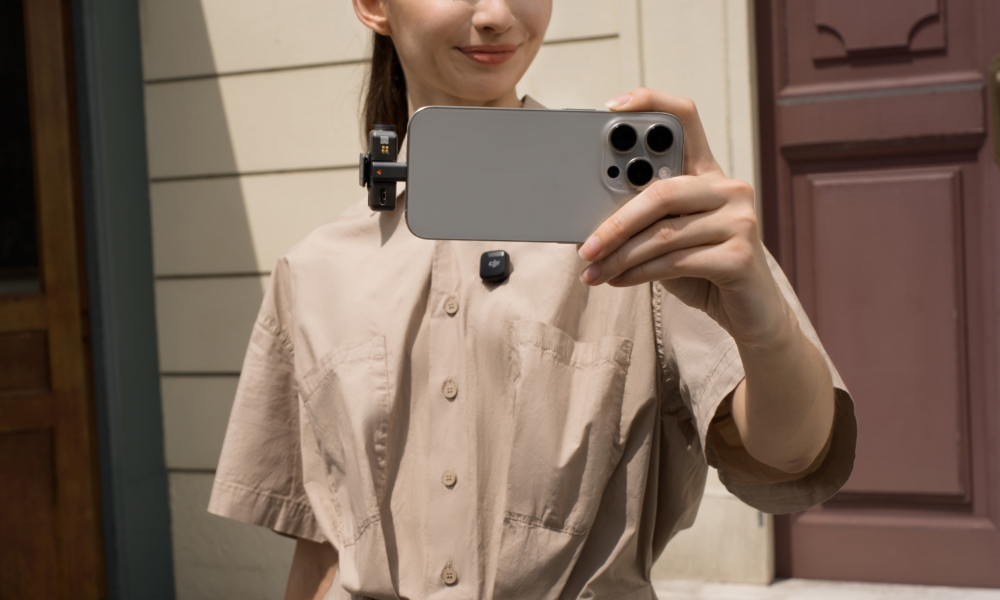 Kobieta trzyma telefon, demonstrując mikrofon. Mały mikrofon jest podłączony do telefonu.