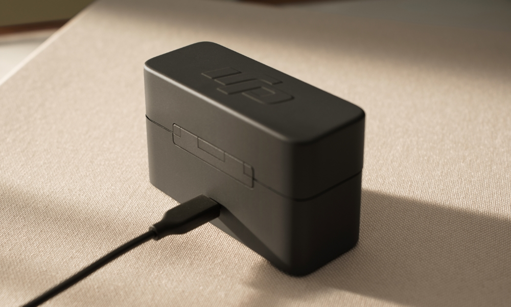 Małe czarne etui ładujące z podłączonym kablem USB-C, na jasnej powierzchni.