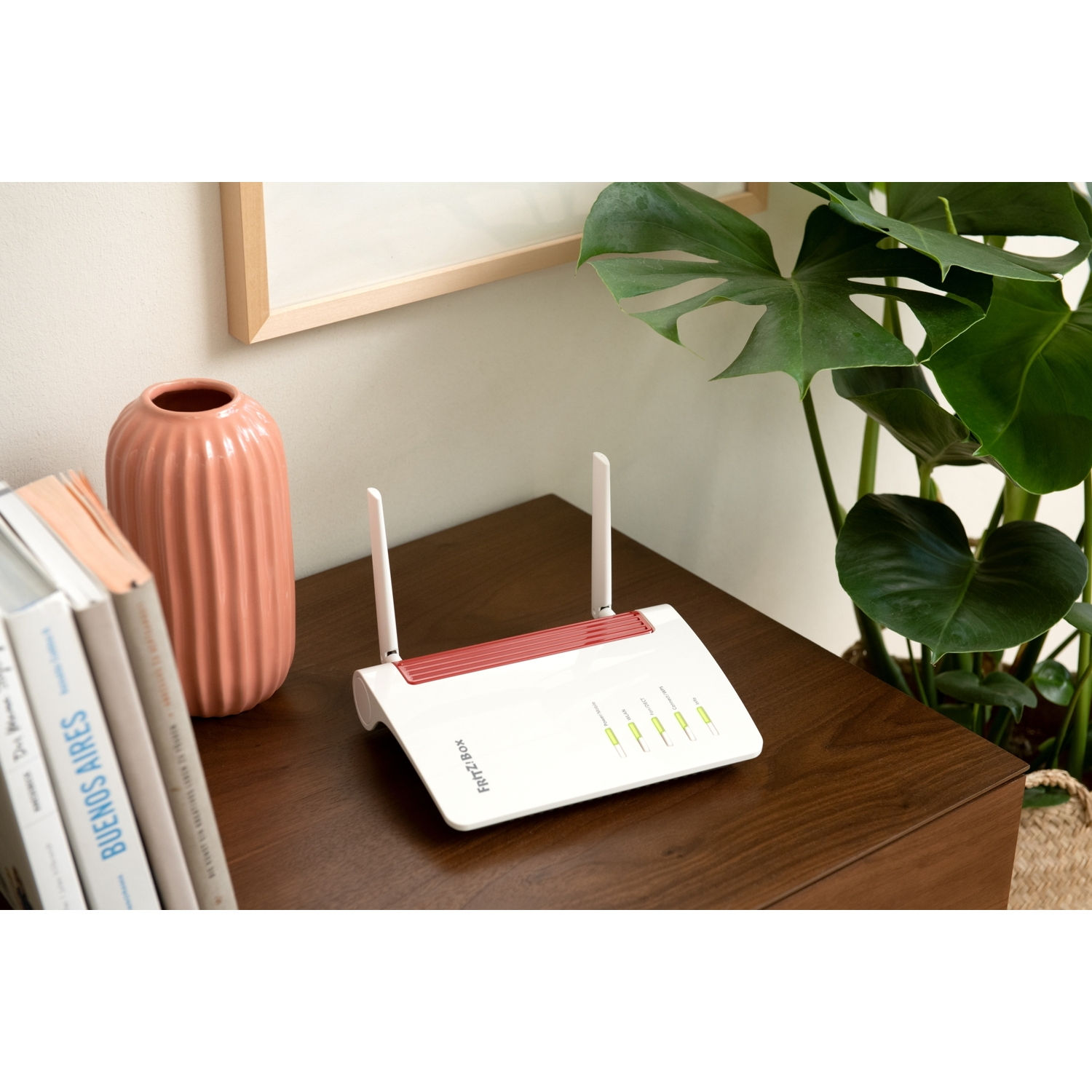 Un routeur blanc avec deux antennes sur une table en bois avec des plantes et des livres.