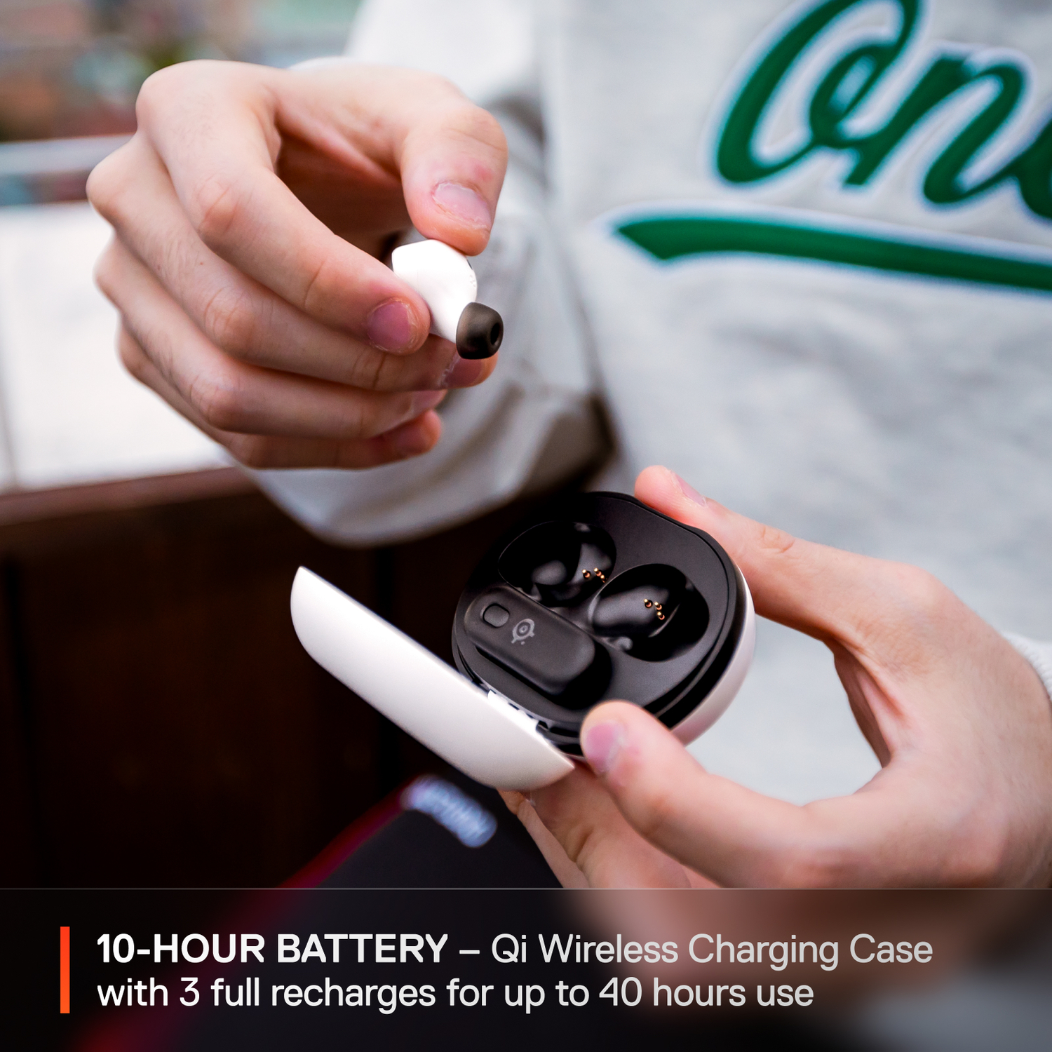 Hands holding a white and black wireless earbud and its charging case.