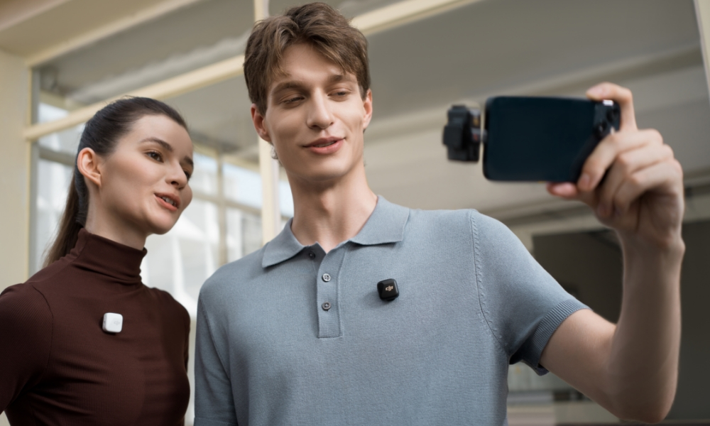 Dwie osoby trzymają smartfon z mikrofonem bezprzewodowym, w pomieszczeniu. Uśmiechnięci.