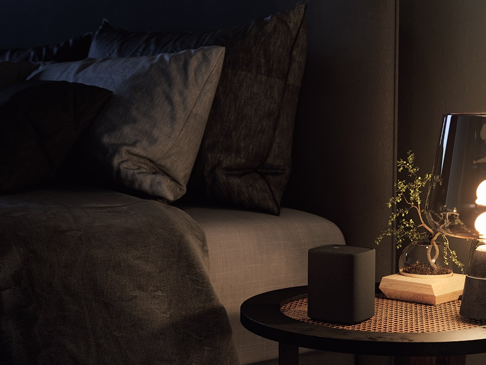 Sypialnia z łóżkiem, poduszkami, stolikiem z lampą i rośliną, ciemna i przytulna sceneria.