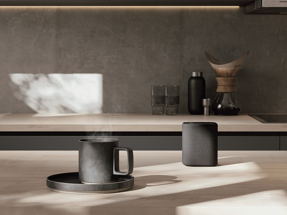 Blat kuchenny z czarnym kubkiem, głośnikiem i innymi przedmiotami.