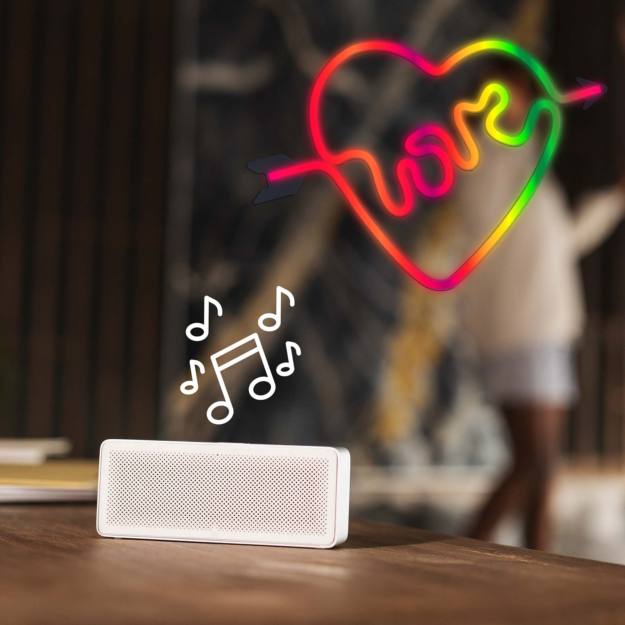 Biały głośnik na drewnianym stole z nutami i neonowym sercem ze strzałą.