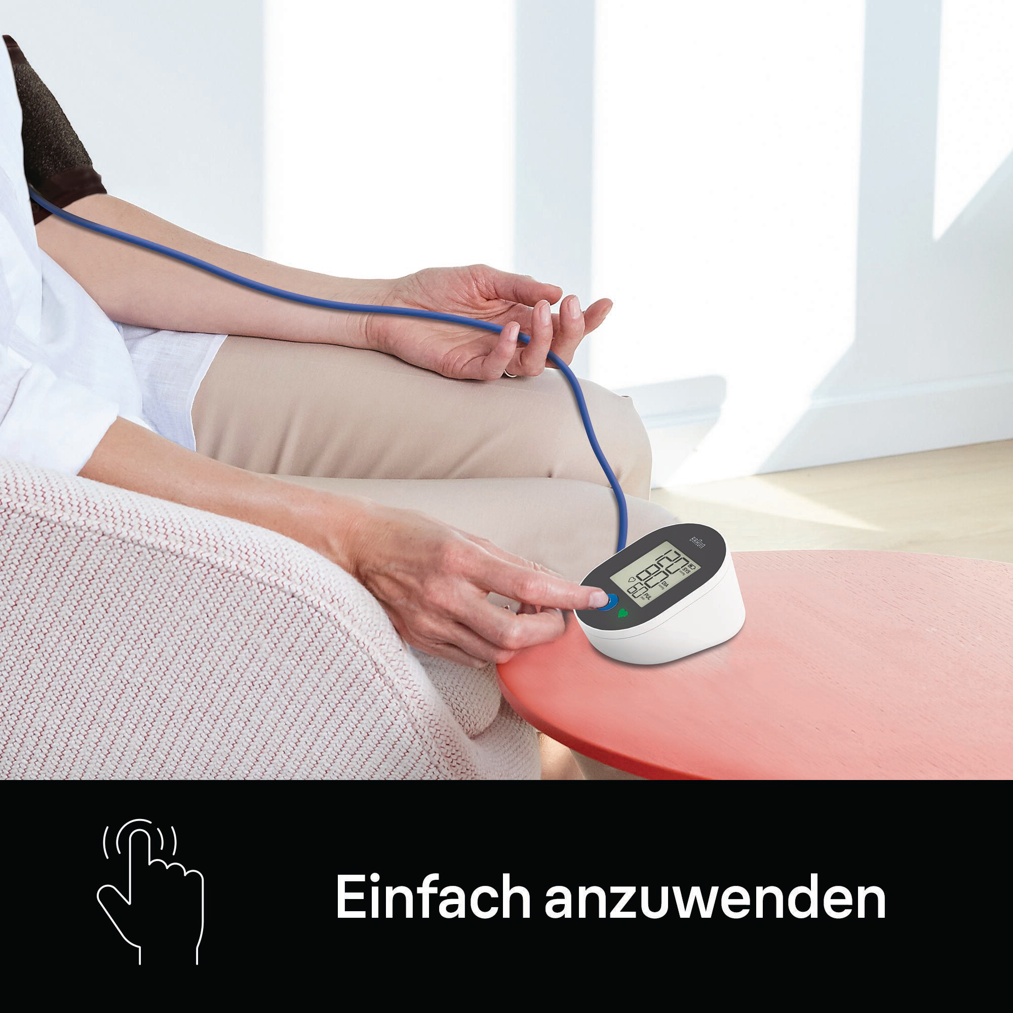 Person misst Blutdruck mit weißem Gerät auf rotem Tisch. Text: 'Einfach anzuwenden'.