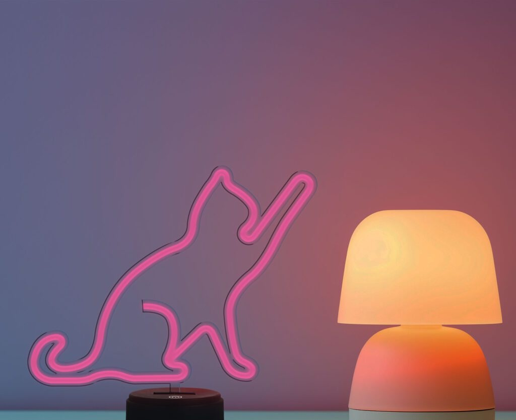Neonowa różowa lampa z sylwetką kota z pomarańczową lampą w pobliżu, na kolorowym tle.