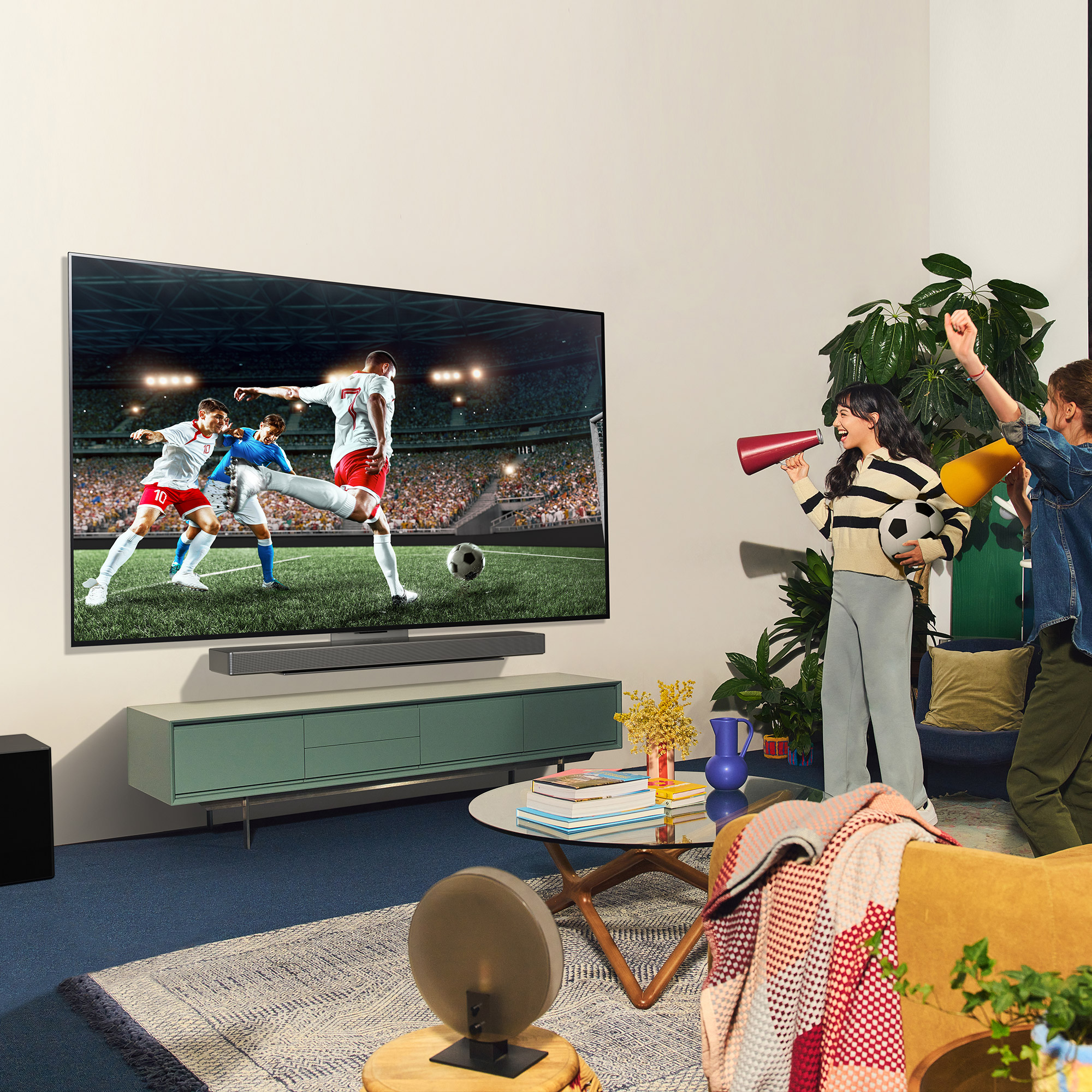 Un televisor grande muestra un partido de fútbol. La gente está viendo el juego, uno con un megáfono, en una sala de estar.