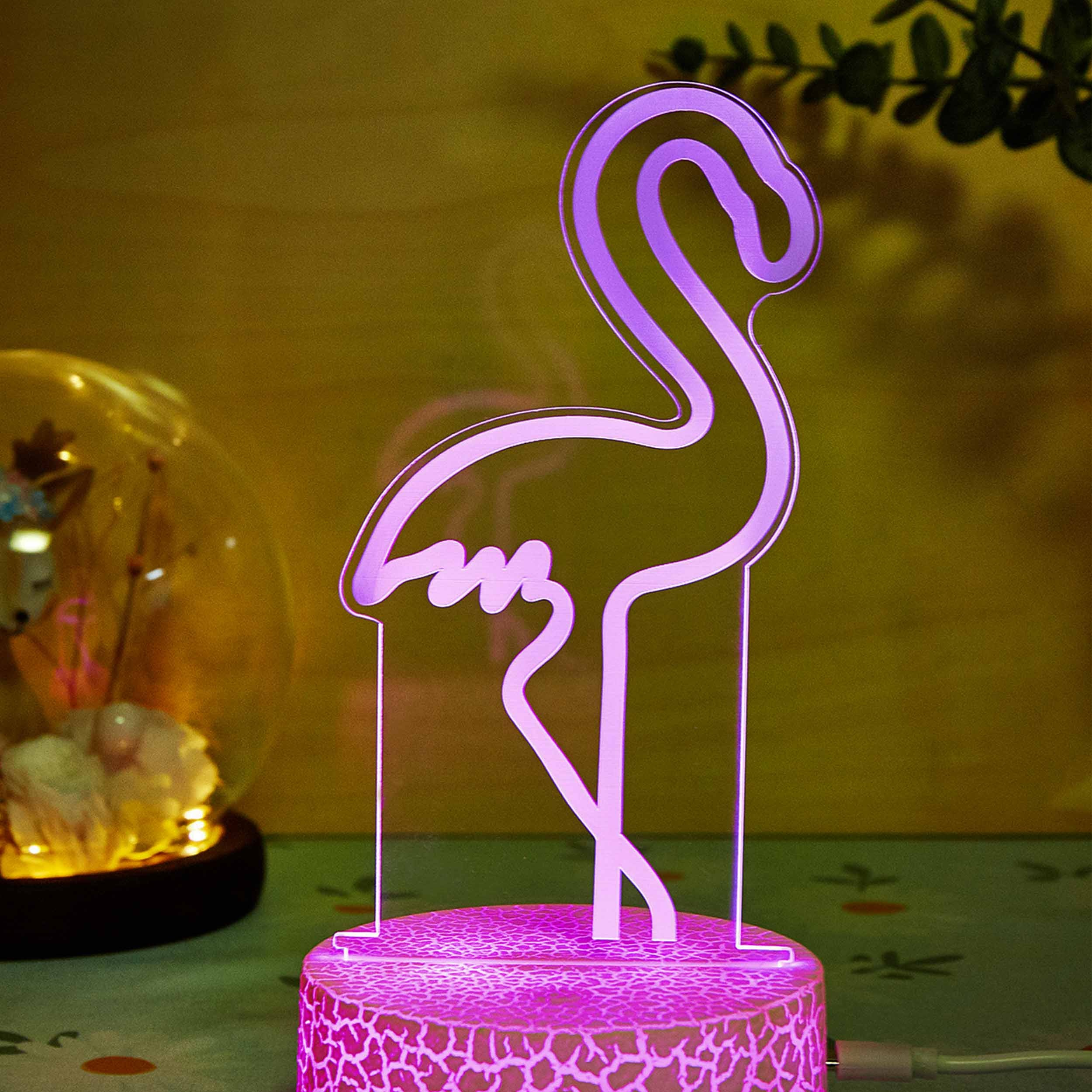 Różowa lampa z konturem flaminga na różowej podstawie, oświetlona różowym blaskiem.