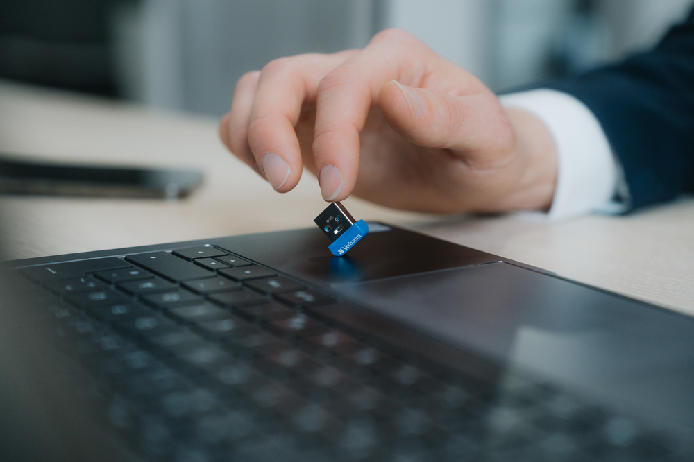 Bir el, mavi Verbatim USB sürücüsünü bir dizüstü bilgisayar klavyesinin üzerinde tutuyor.