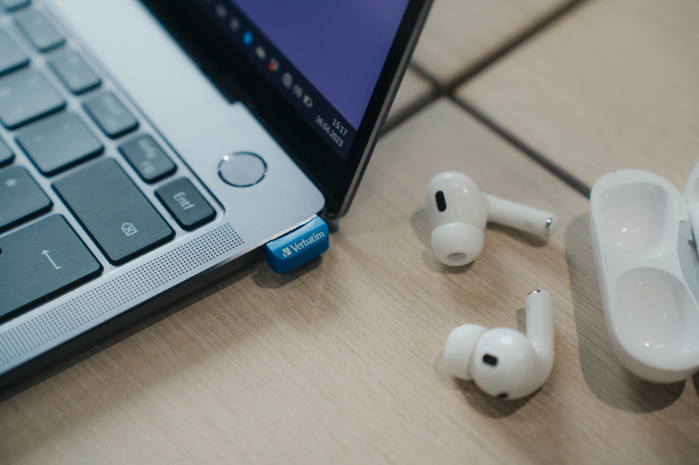 Ahşap bir masada USB ve beyaz kulaklıklarla dizüstü bilgisayar. Arka plan bulanık.