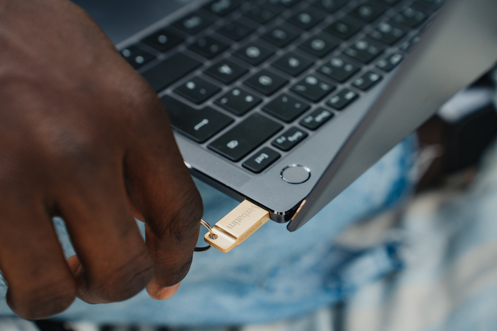 Bir el, altın bir USB sürücüsünü bir dizüstü bilgisayara takıyor, yakın çekim.