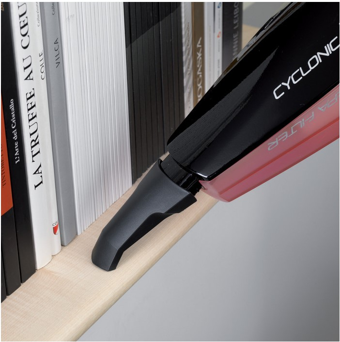 Odkurzacz ręczny czyszczący półkę z książkami. Czerwono-czarne urządzenie, drewniana półka.