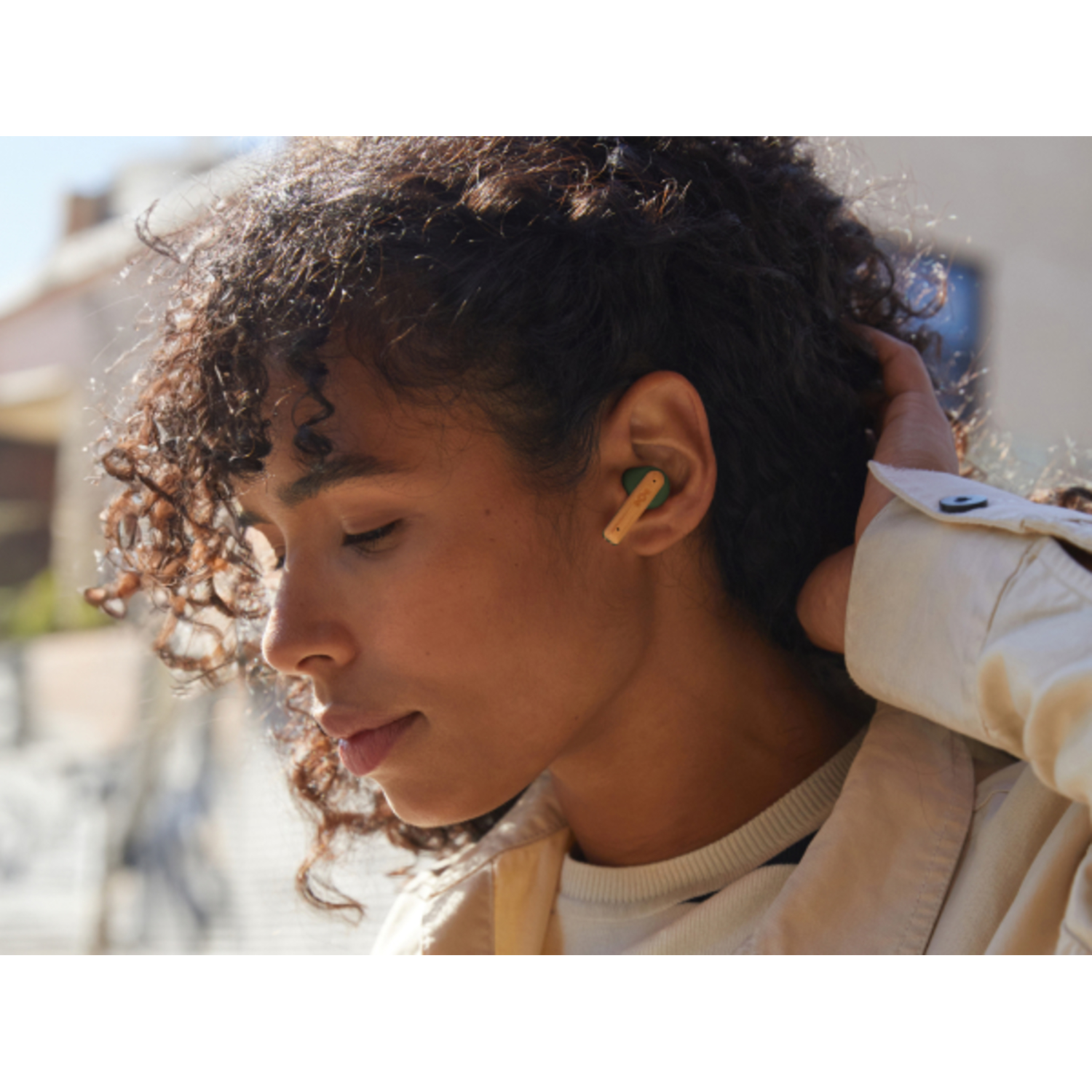 A woman wearing a white jacket, with a yellow and green earbud in her ear.