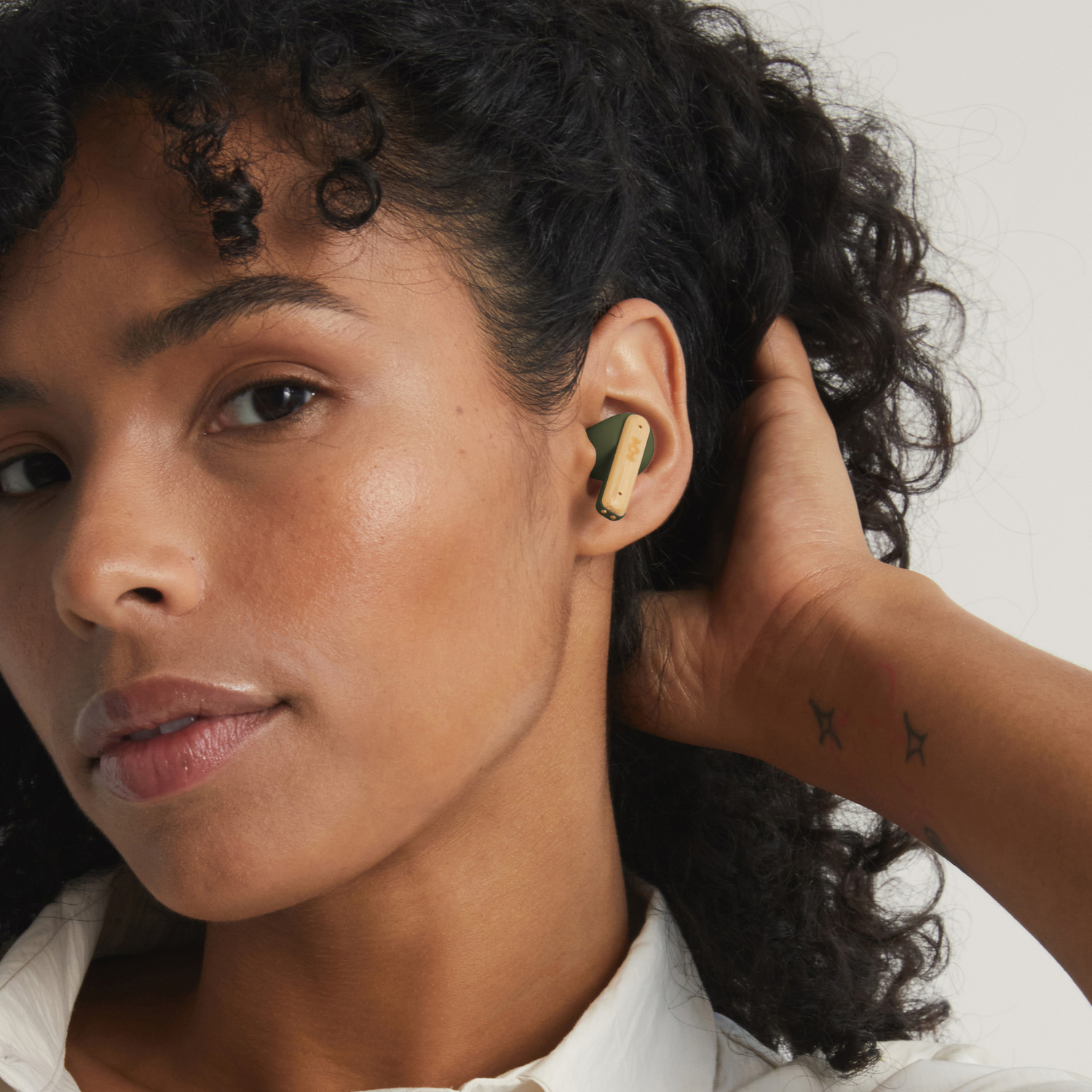 Woman with earbuds in her ears. One earbud is gold and green.