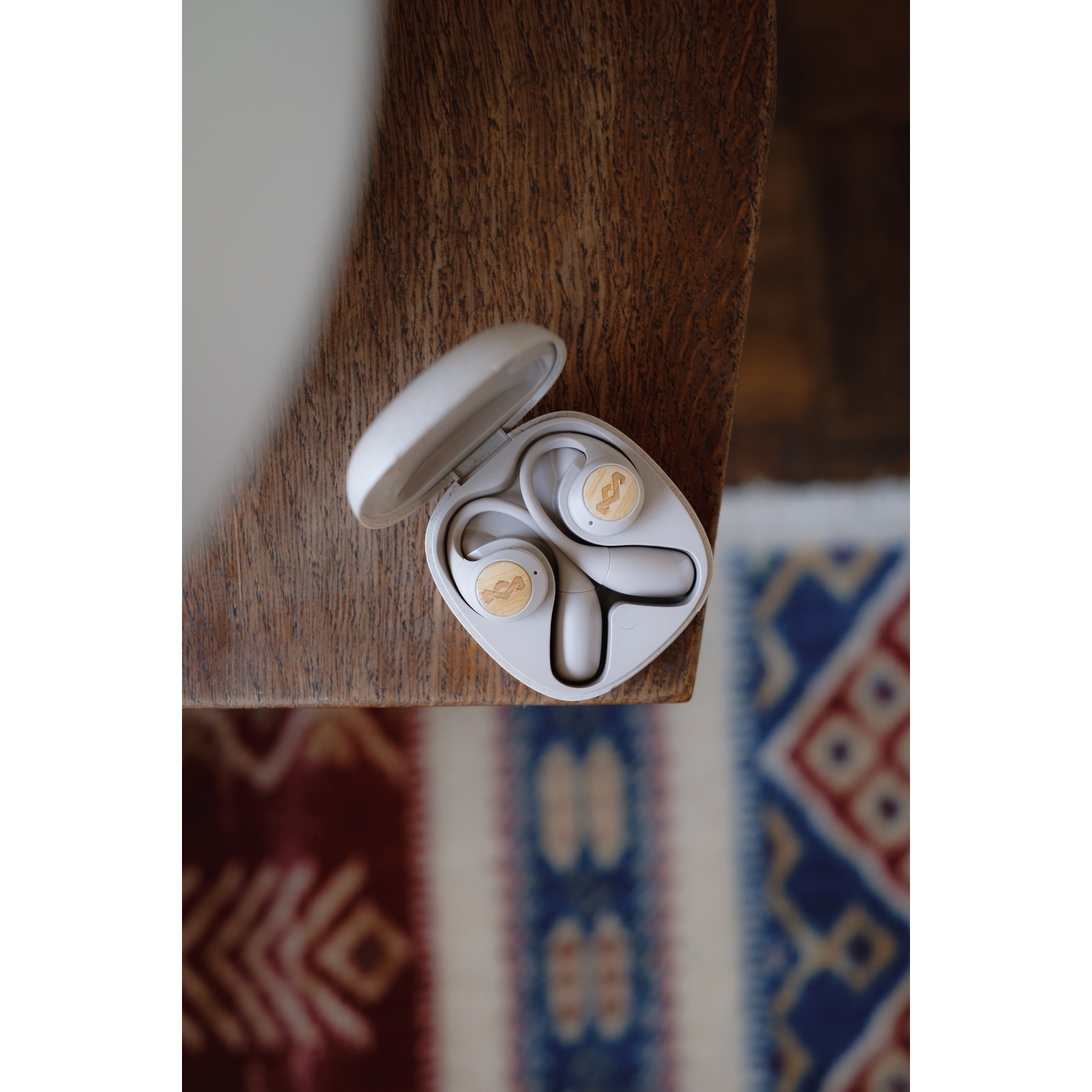 Étui d'écouteurs blanc ouvert, avec écouteurs à l'intérieur, sur table et tapis.