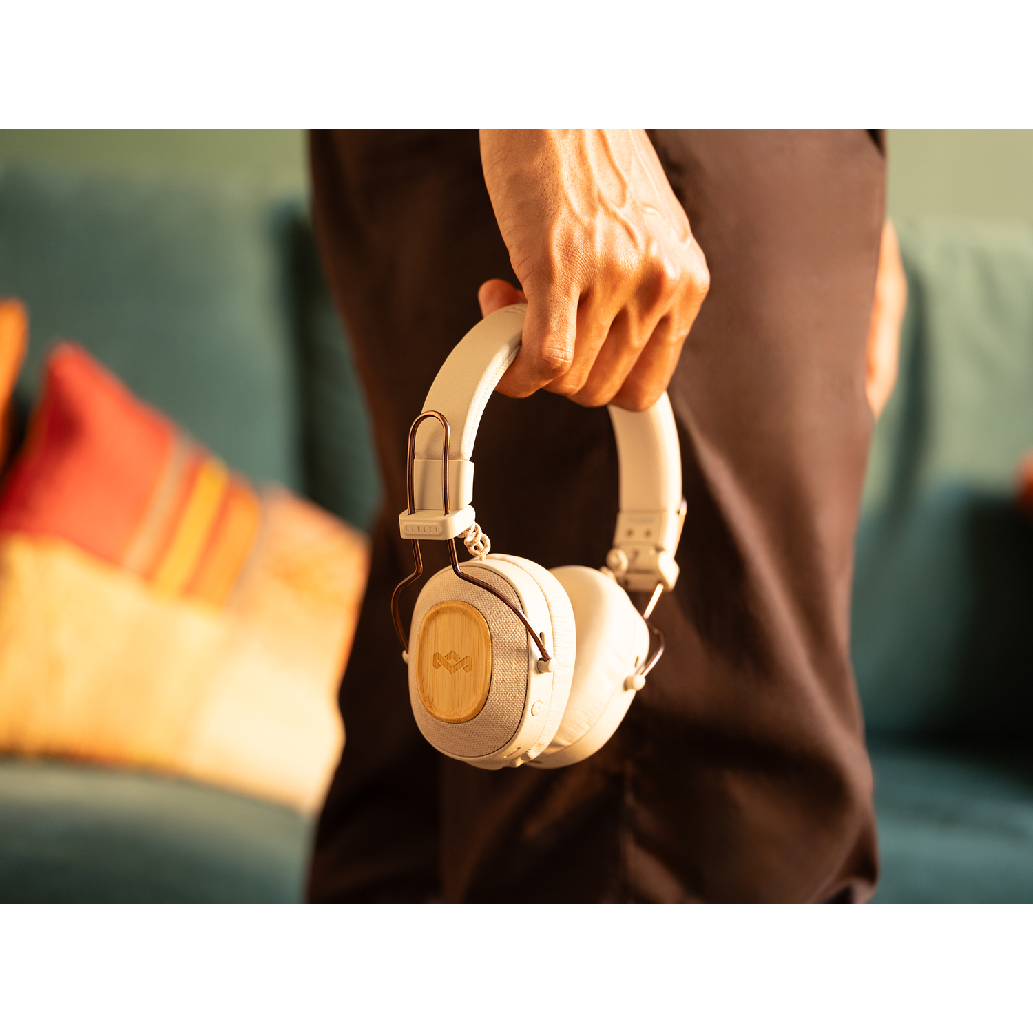 Une personne tient un casque beige. L'arrière-plan montre un canapé et un mur vert.