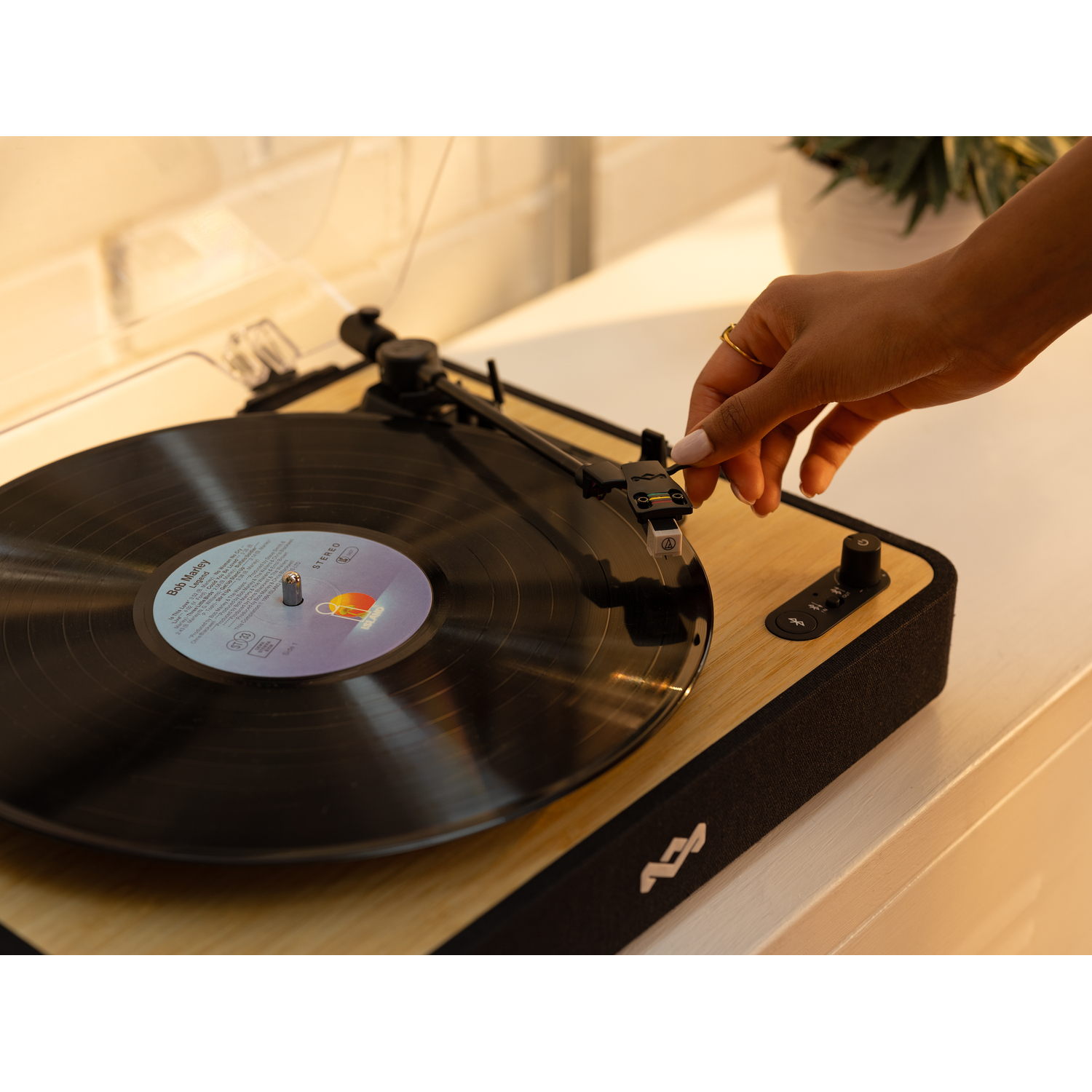 A person's hand placing the needle on a vinyl record on a wooden record player.