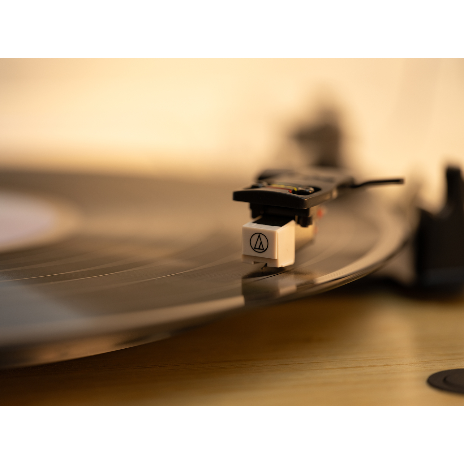 Close-up of a record player with a black arm and white cartridge playing a vinyl record on a wooden surface.