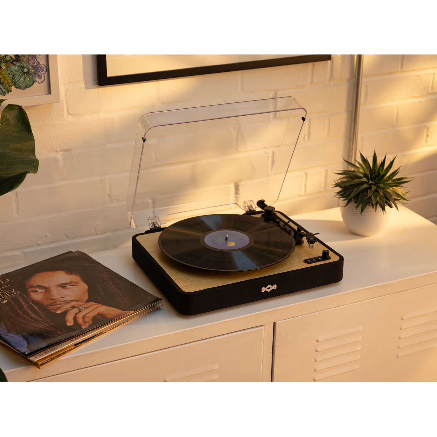 A record player on a white table. A vinyl record is on the player, next to a record sleeve.