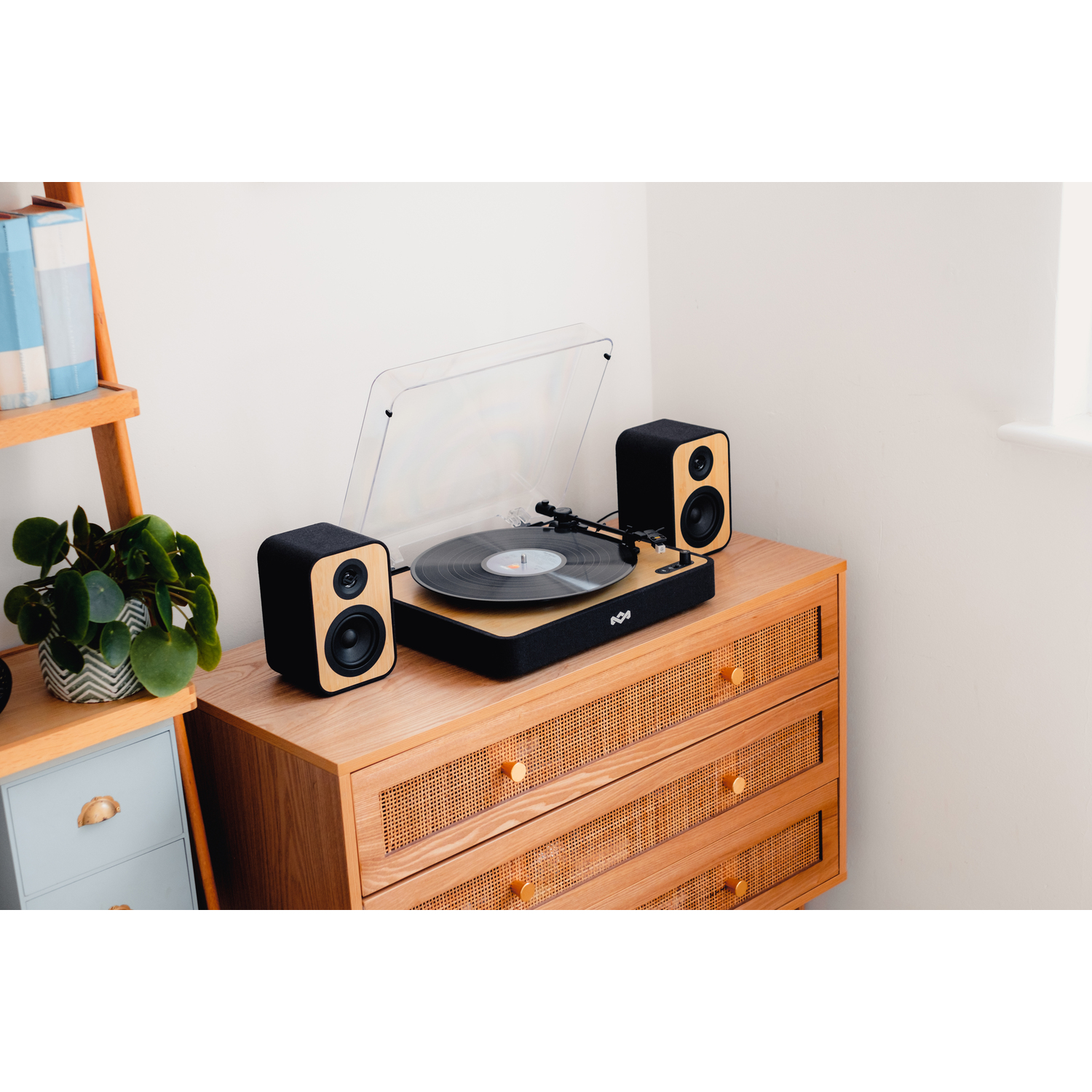 Een platenspeler met luidsprekers op een houten kast. Een plant en boeken op een plank links.