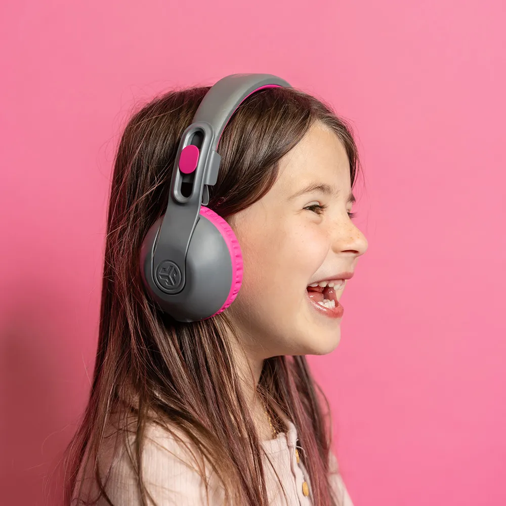 Ragazza con cuffie grigie e rosa, sorridente, vista laterale, sfondo rosa.