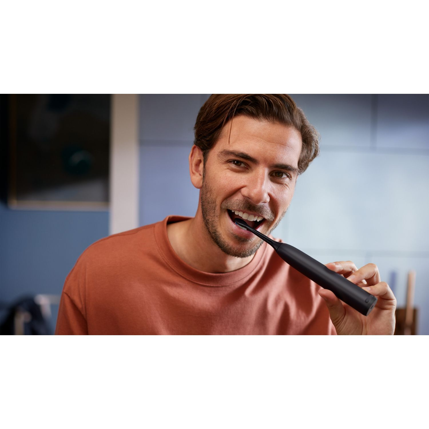 Homme se brossant les dents avec une brosse à dents électrique noire. Il sourit.