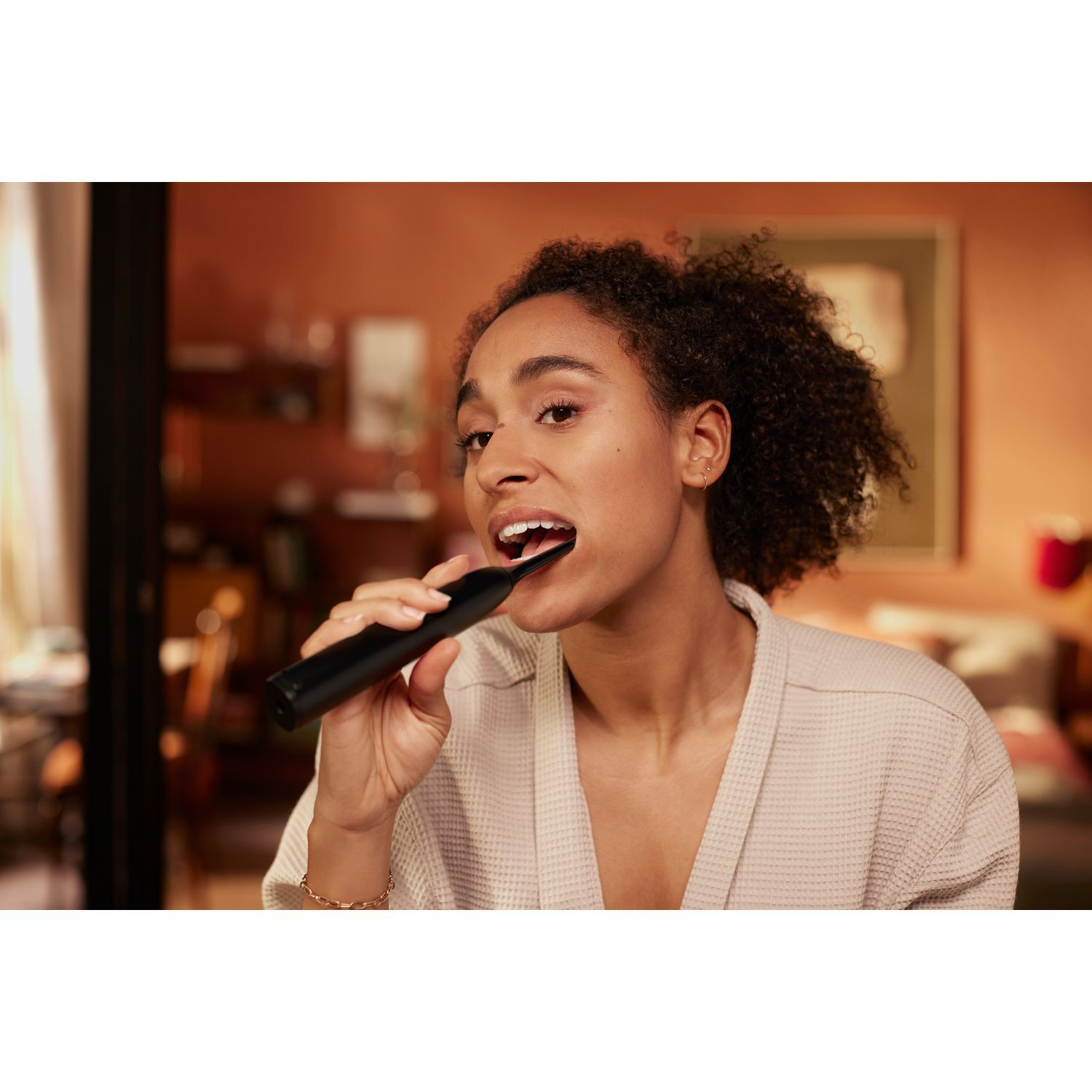 Femme se brossant les dents avec une brosse à dents électrique noire. Fond chaud.