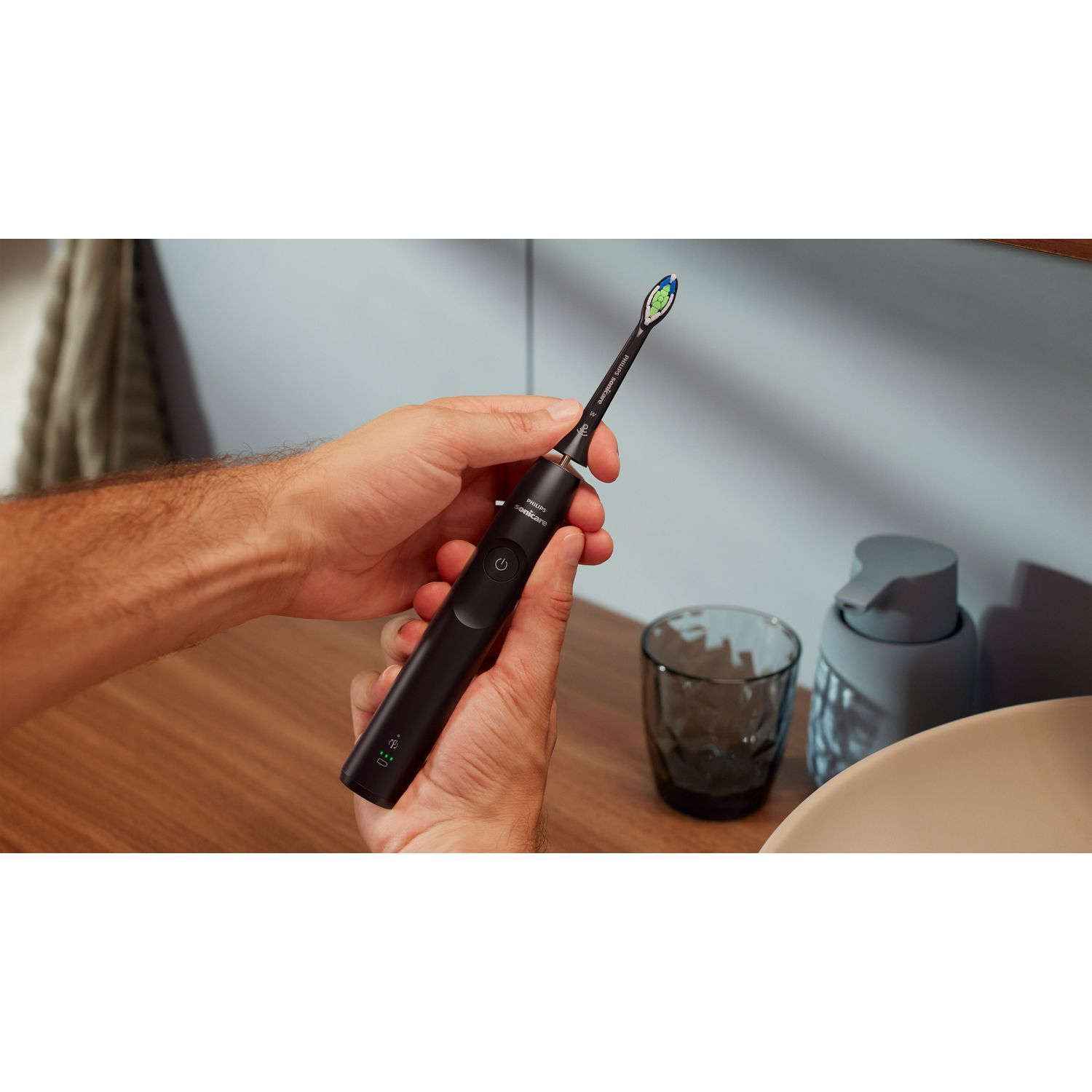 Mains tenant une brosse à dents noire à côté d'un évier.