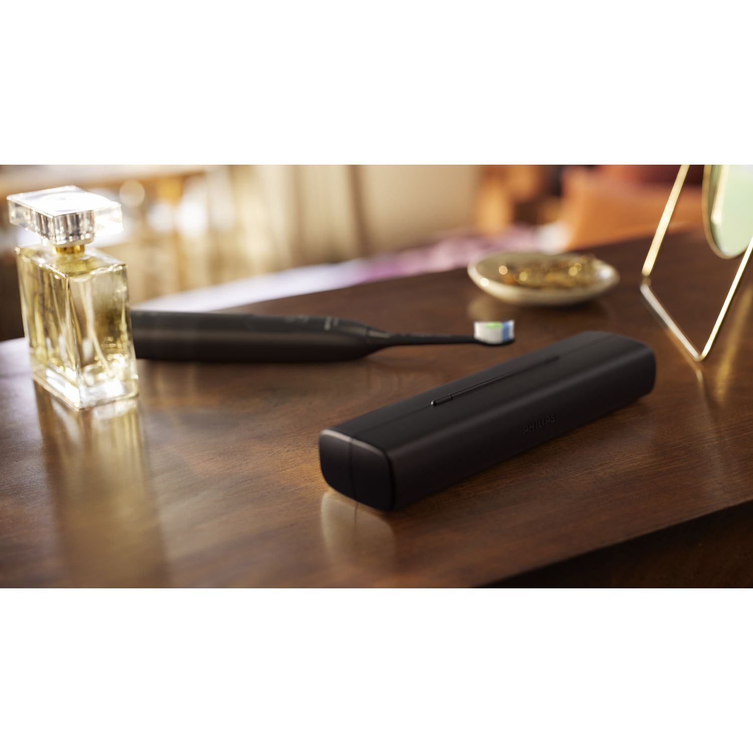 Étui et brosse à dents noirs sur une table en bois. Un flacon de parfum est également visible.