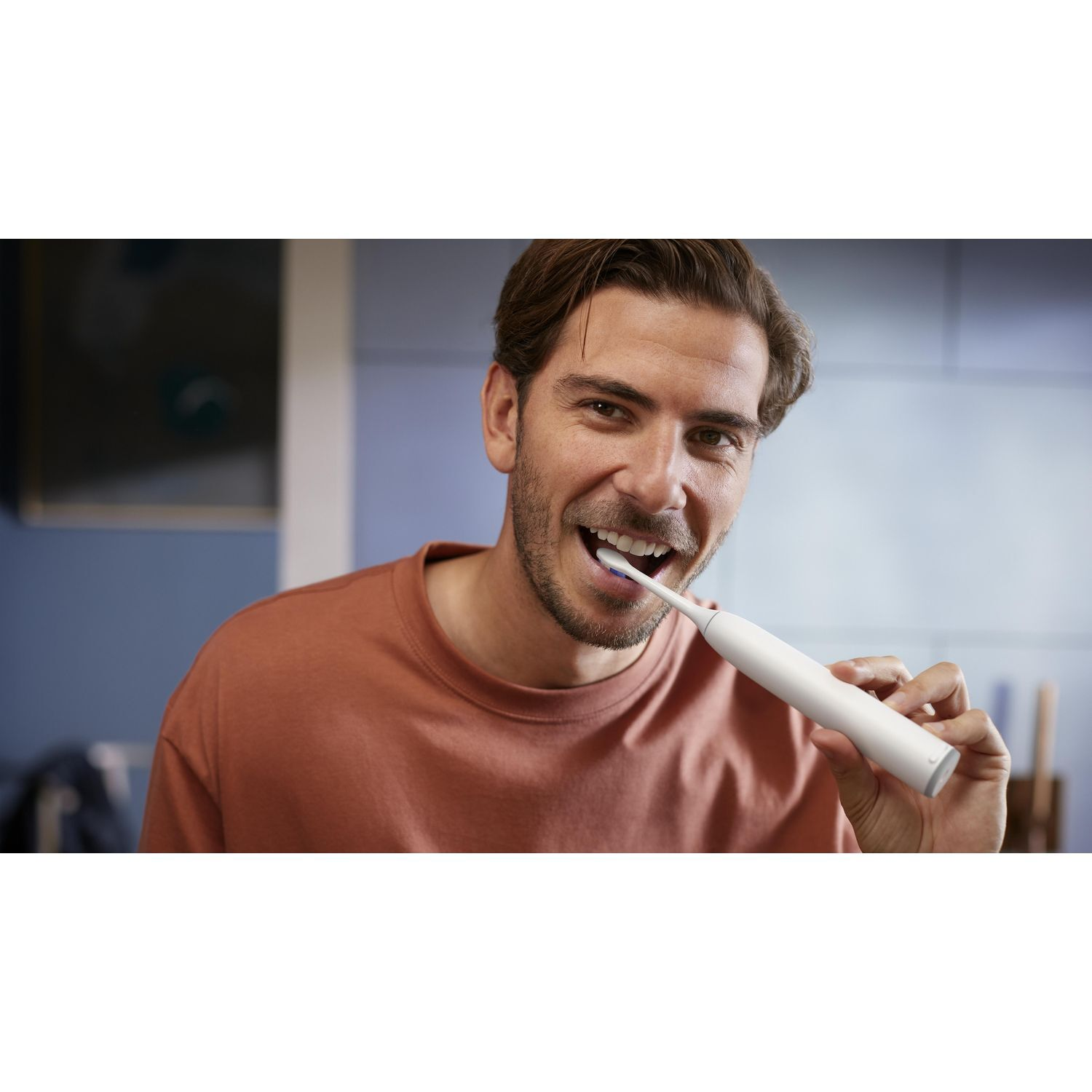 Un homme avec une chemise marron se brosse les dents avec une brosse à dents électrique blanche.